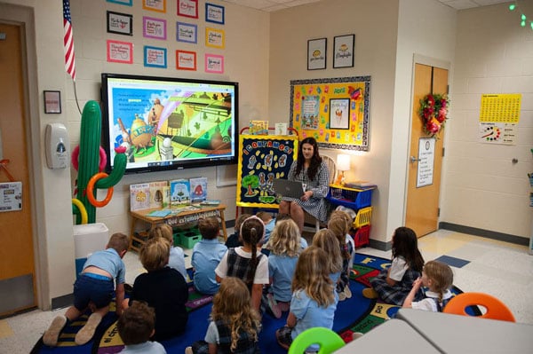 A lower school classroom with children sitting on the floor doing an interactive activity.