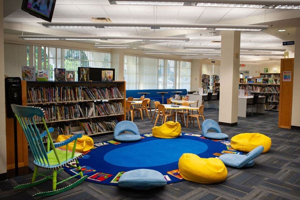 A library with a rocking chair and bean bags around a blue rug.
